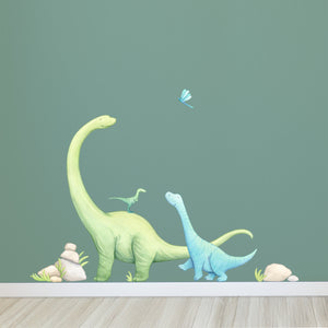 Wall decals of three dinosaurs on a green wall with rocks.