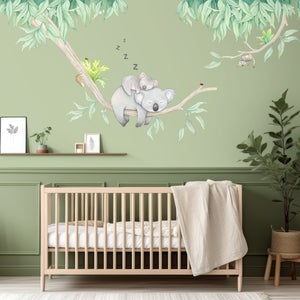 Children's room with a crib, wall decals of koalas on a branch, and green walls.